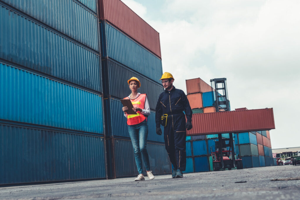 Industrial worker works with co-worker at overseas shipping container yard . Logistics supply chain management and international goods export concept